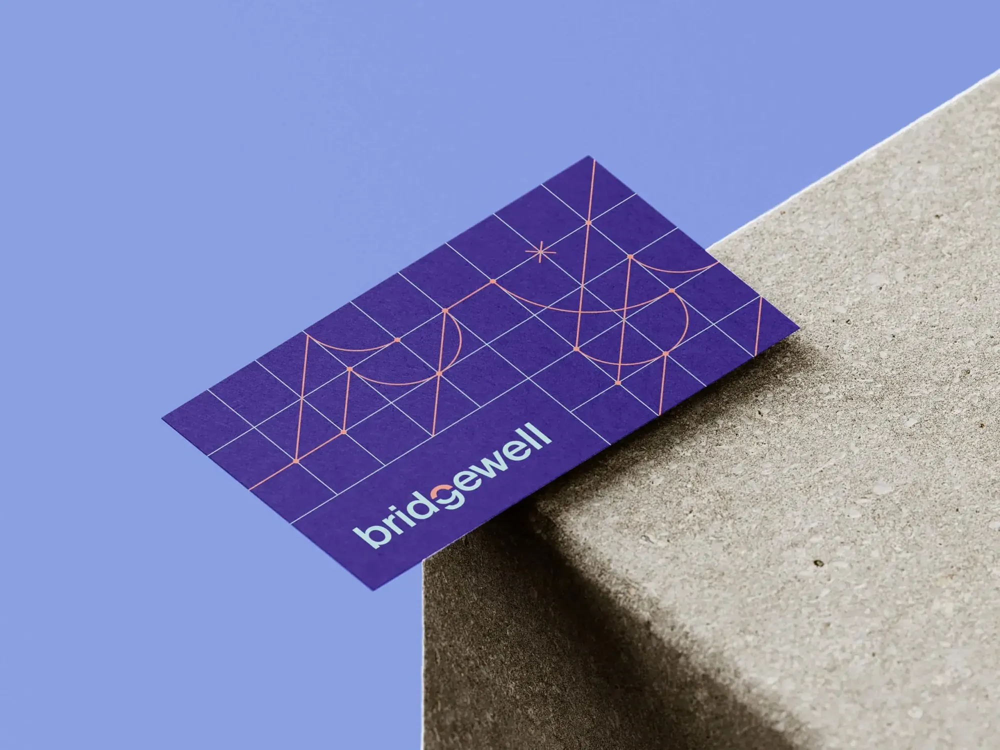 Purple Bridgewell business card with a fine gold line pattern, resting on a stone ledge