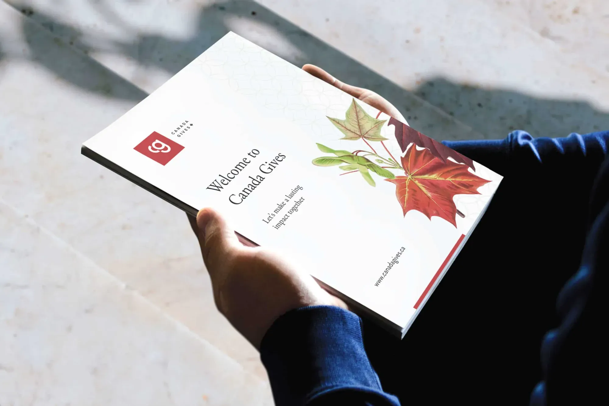 Canada Gives welcome guide with a red maple leaf illustration, held open in two hands