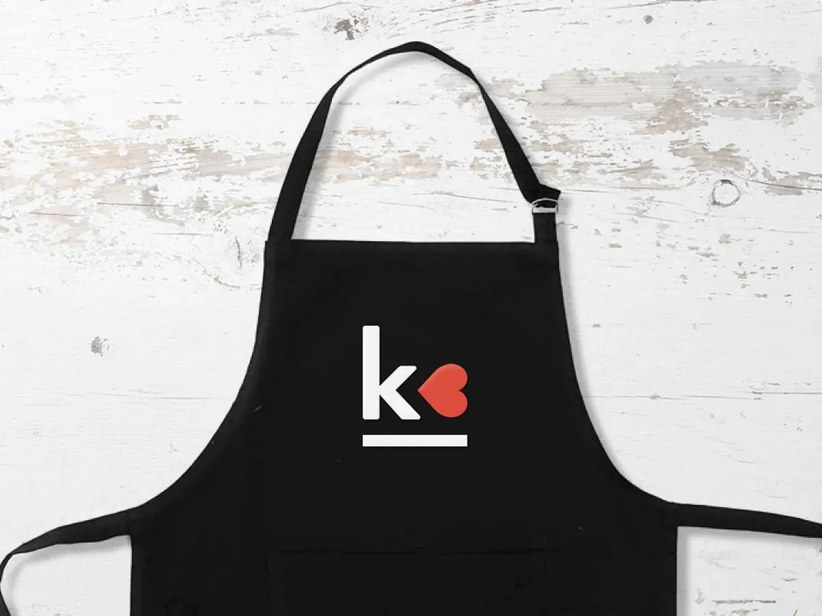 Black apron printed with the KTC logo, a white k beside a red heart
