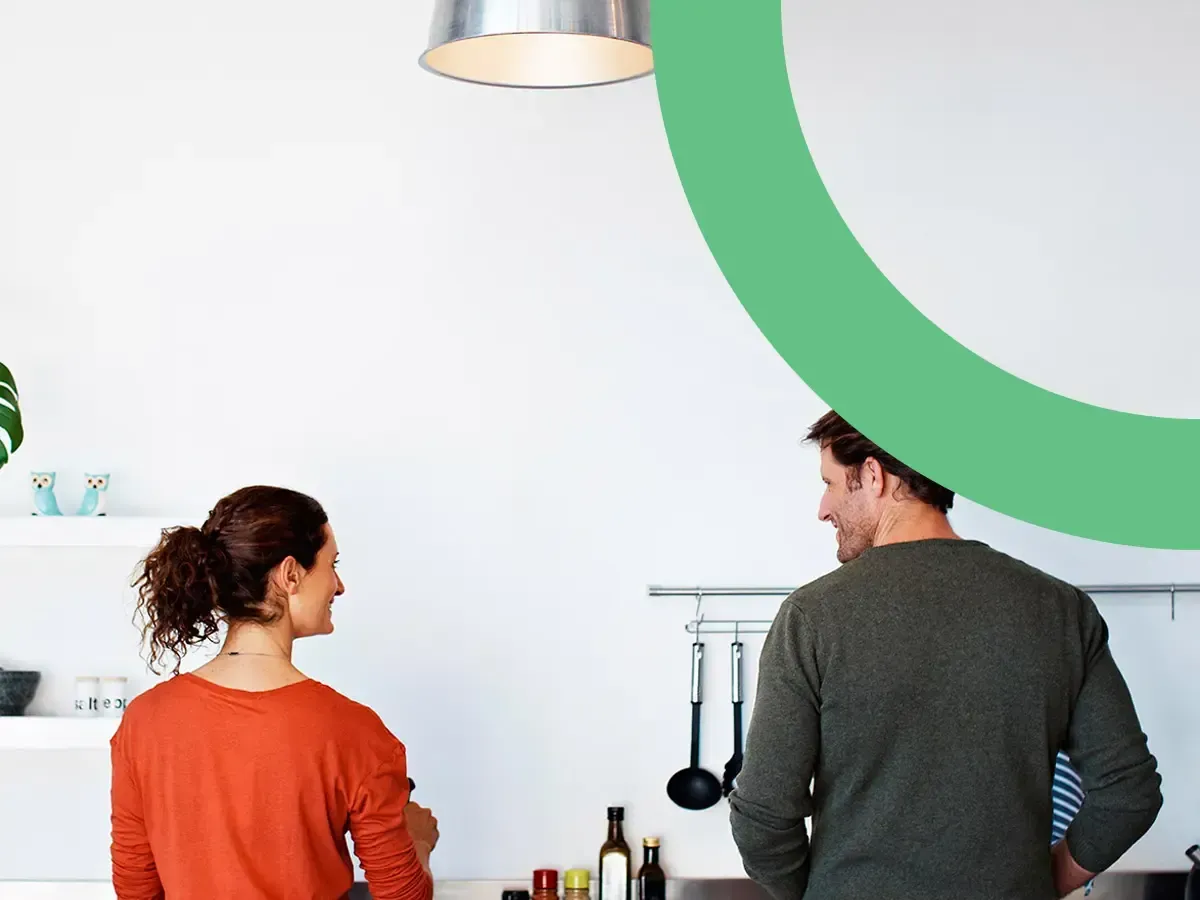 Couple standing in a bright kitchen beneath a large green brand arc