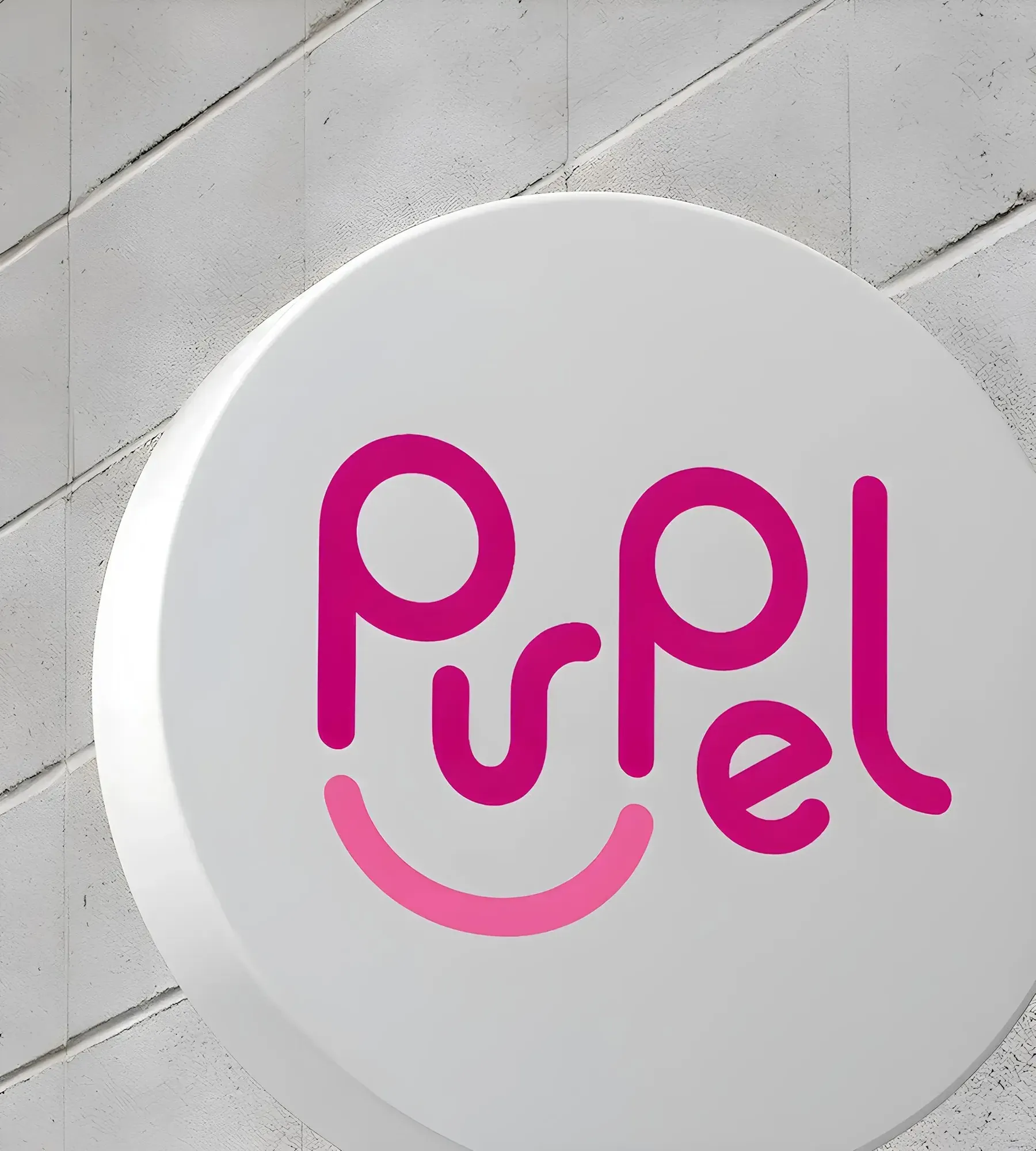 Purpel logo in pink with a smile-shaped underline on a round white wall sign